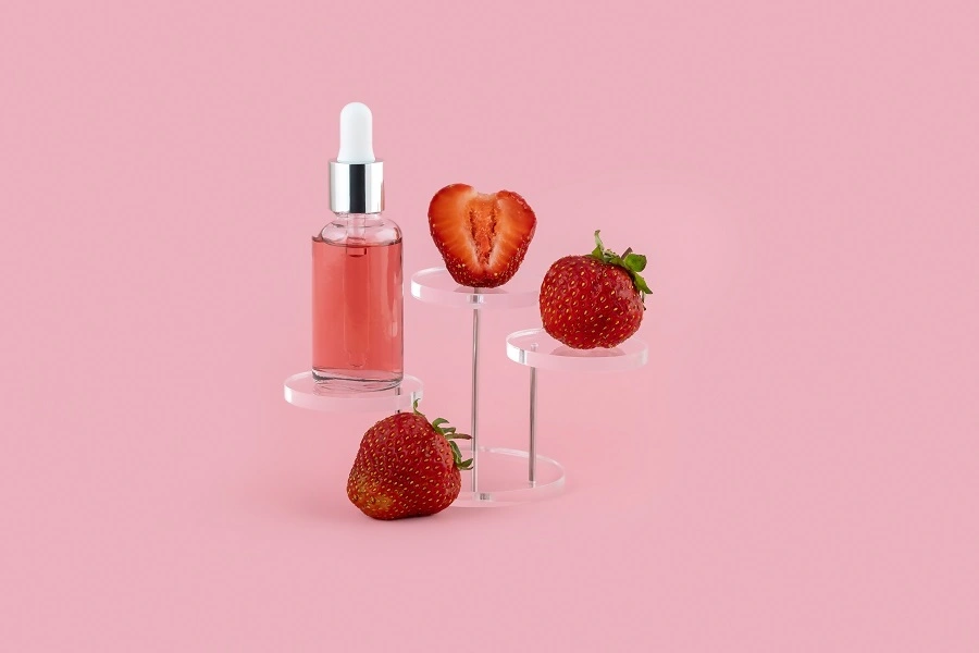 three half cut strawberries on a stand with pink liquid in a transparent bottle against pink background